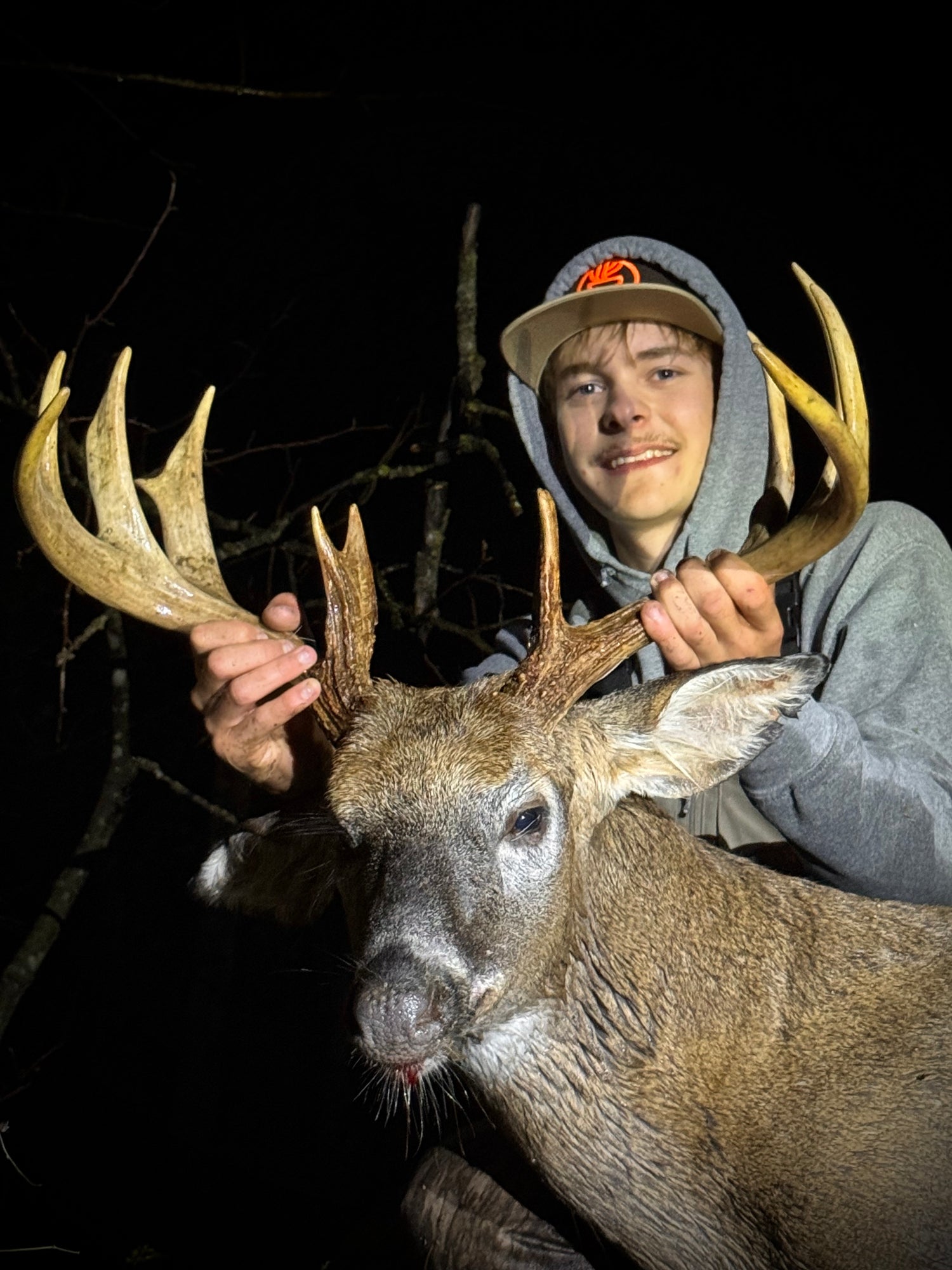 Person holding a large deer with prominent antlers at night.